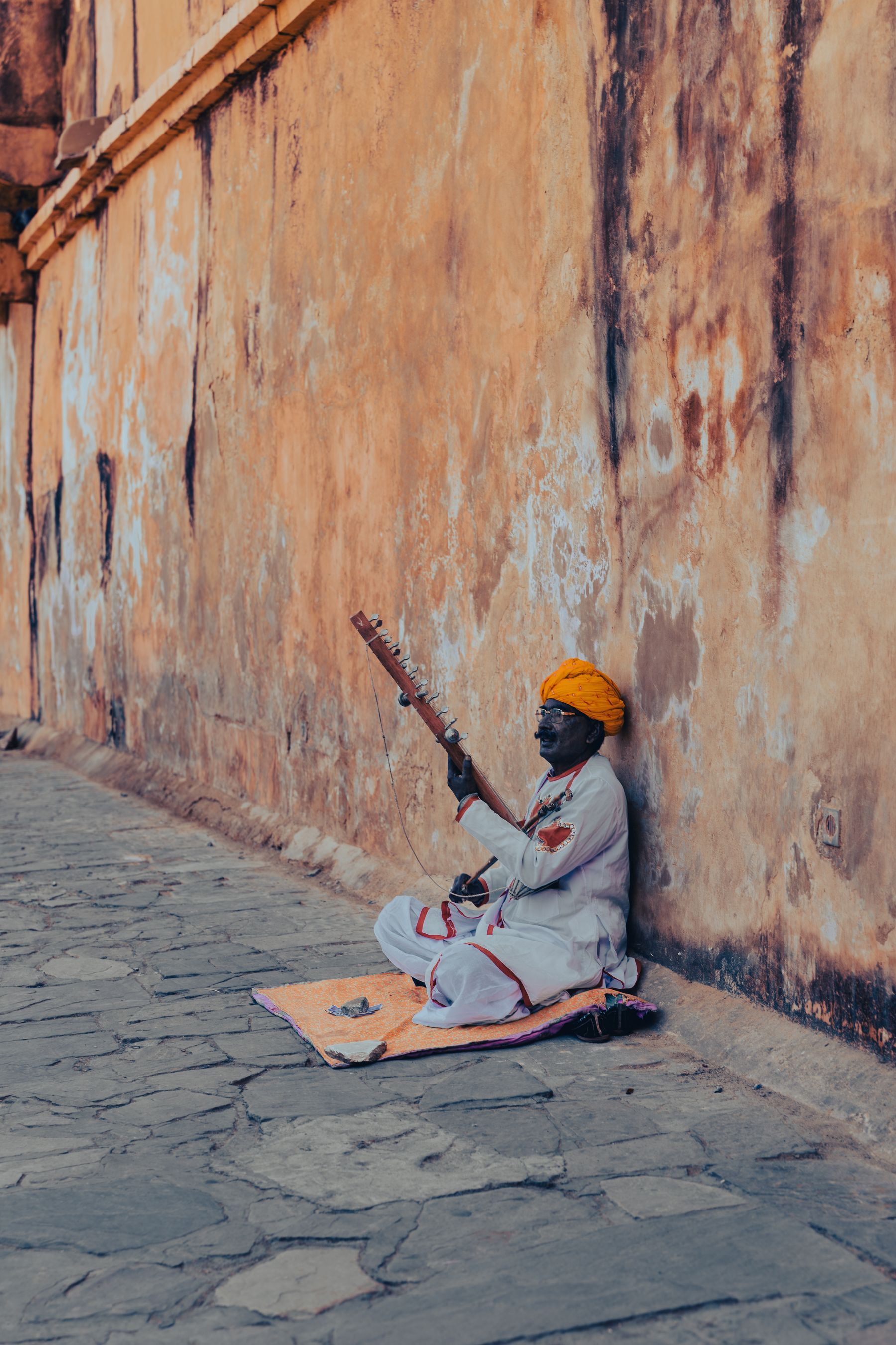 Seated Musician In Orange Turban Against Weathered Wall